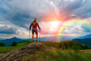 山頂で虹と日の入りを見つめる登山者