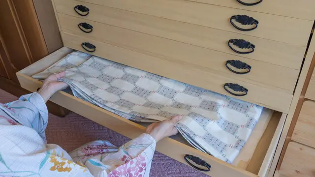 桐の箪笥に着物生地をしまう女性