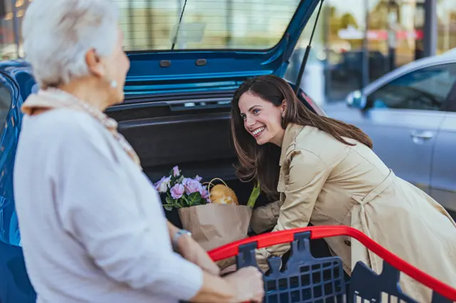 高齢の女性が買物した荷物を車へ積んであげている女性